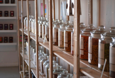 Multiple glass containers filled with dry food items on wood shelves in a store