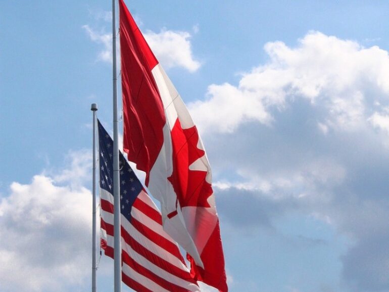 canadian and united-states flags blowing in the wind side by side