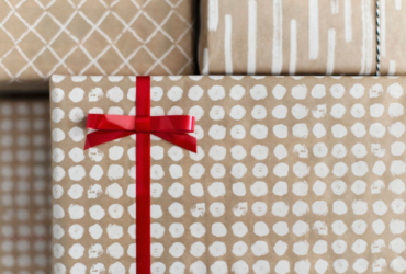 Holiday gifts in light brown wrapping with white pattern and a red bow tied on.